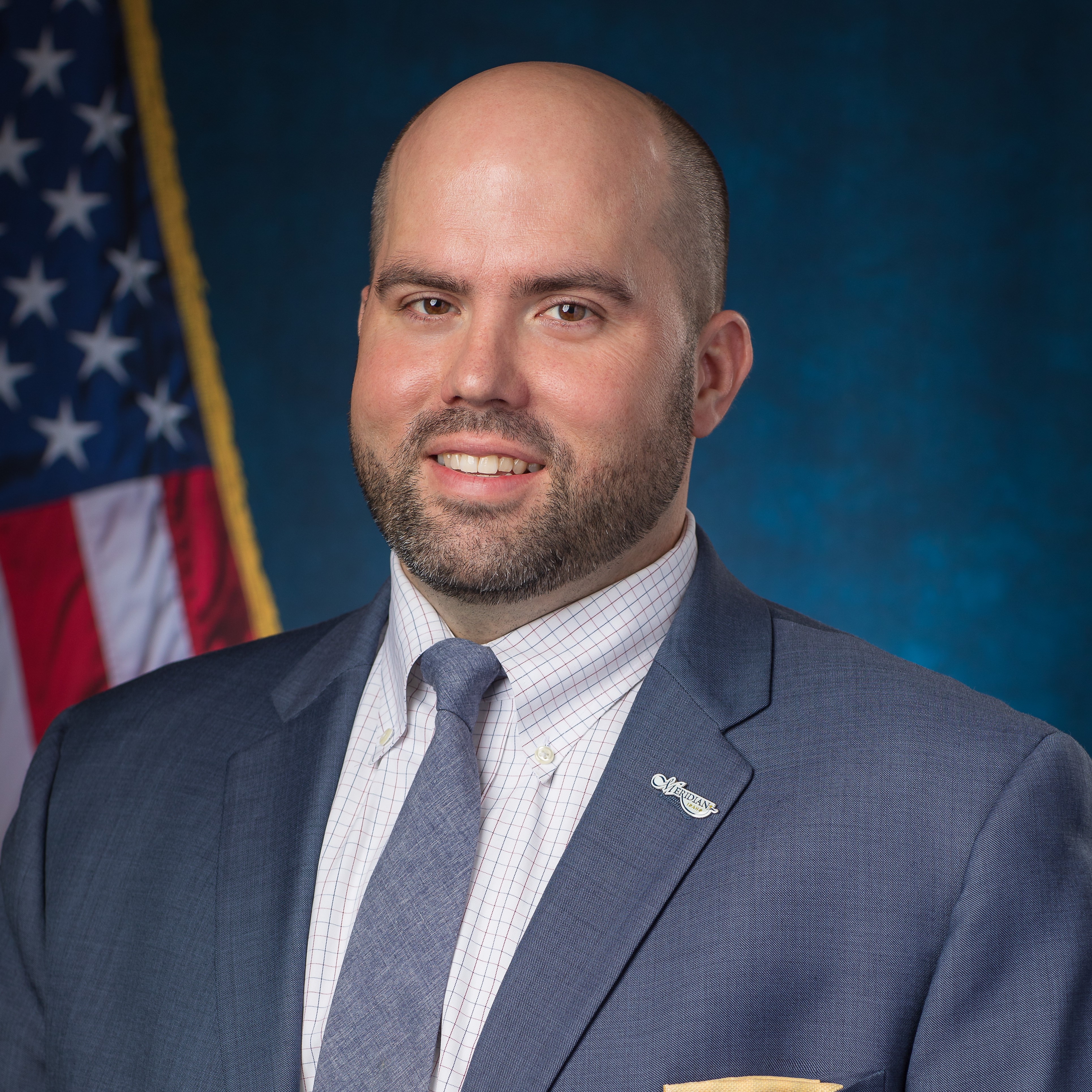 Councilor Luke Cavener in front of blue background and U.S. flag.