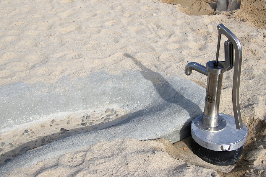 Hand operated water pump, concrete streambed and sand in sand and water play area at Discovery Park