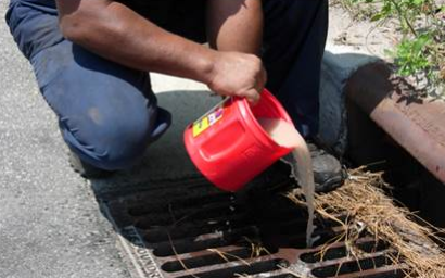 Photo of a cloudy liquid being poured from a red container into a storm drain